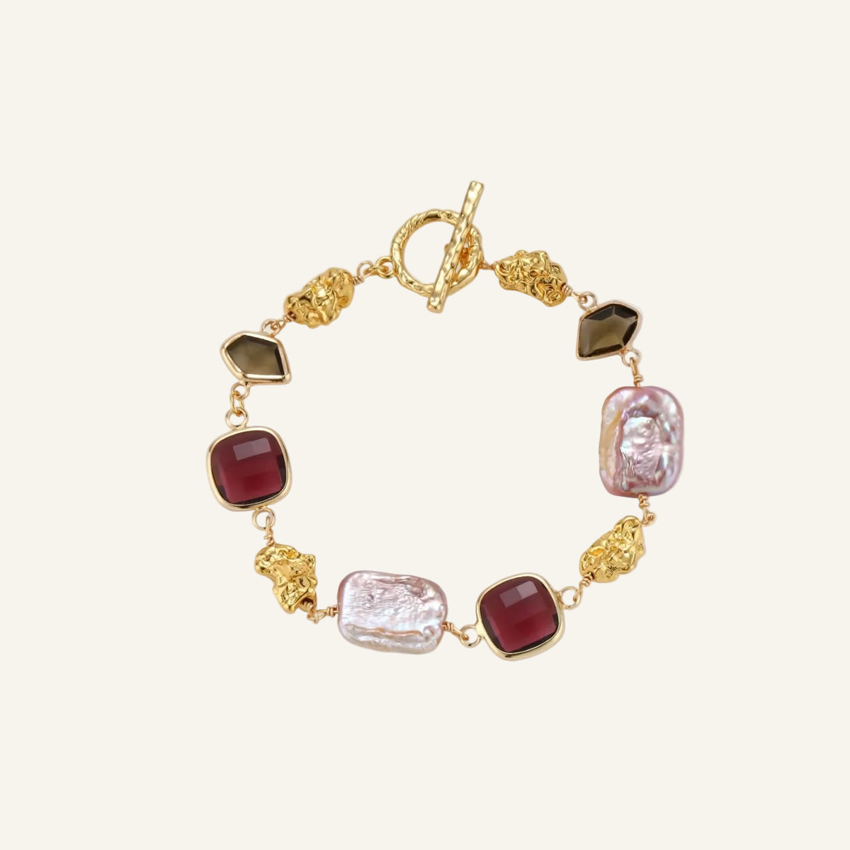 18k gold-plated copper bracelet with burgundy stones, smoky quartz, baroque pearls and ornate golden charms on white background.