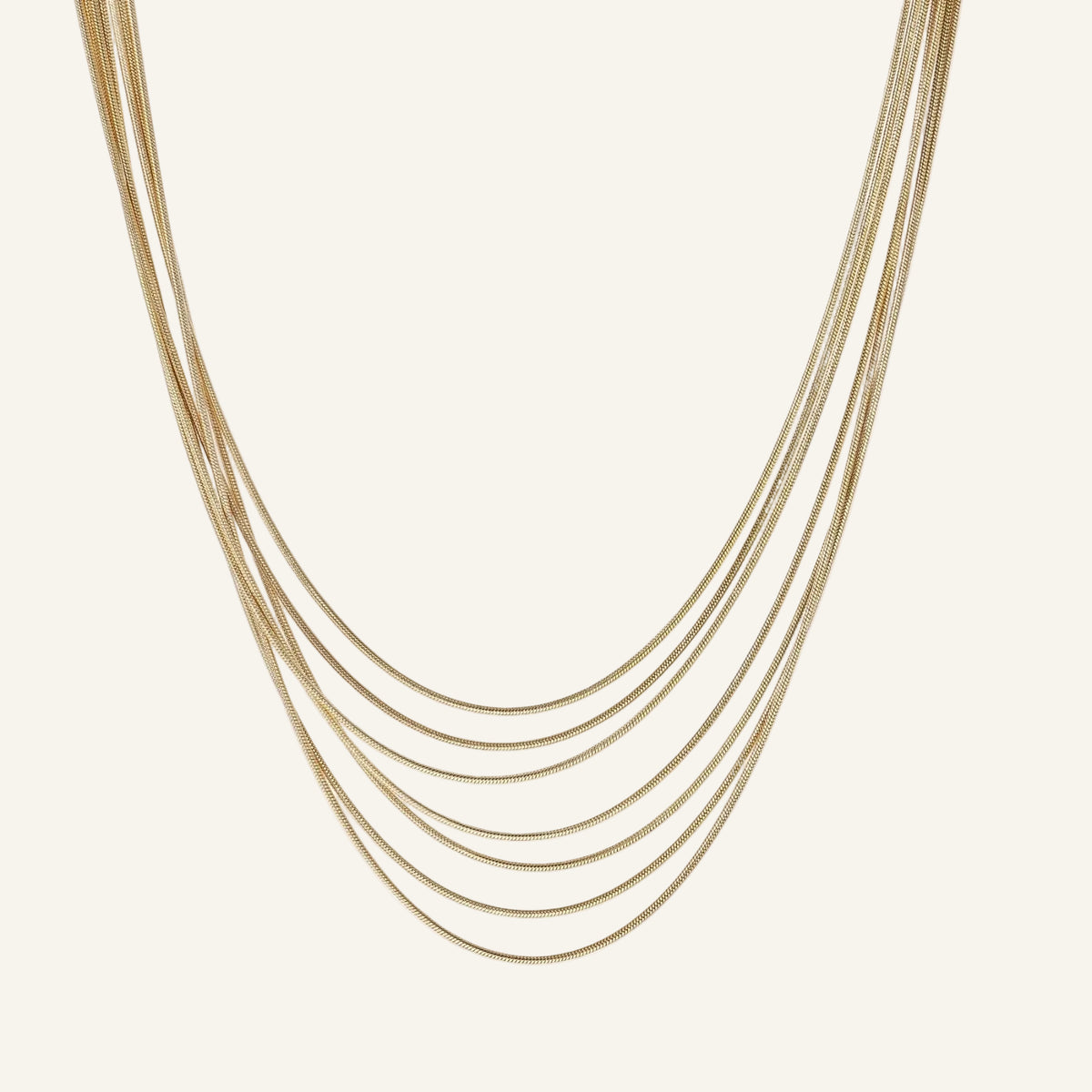 Seven delicate gold-plated snake chains create an elegant layered necklace on a neutral background.