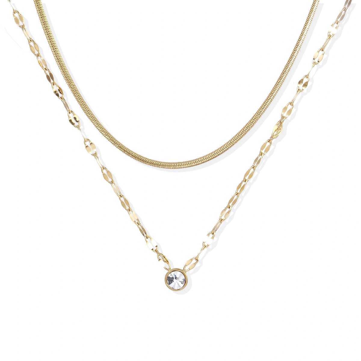 Layered gold necklace with herringbone and link chains, small bezel-set crystal pendant on cream background