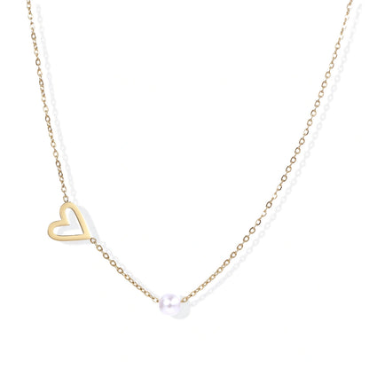 Delicate gold necklace with open heart charm and white pearl bead on fine chain against cream background