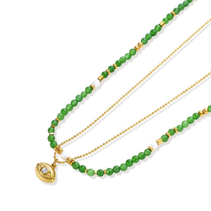 Layered necklace with green stone beads, gold spacers, white accents, and protective eye pendant on cream background.