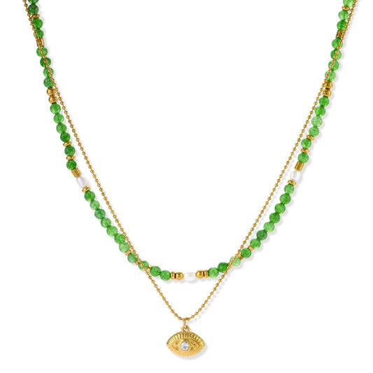 Layered necklace with green stone beads, gold spacers, white accents, and protective eye pendant on cream background.