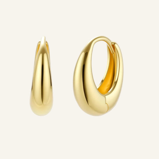 Chunky gold-plated sterling silver huggie hoop earrings with hinged closure mechanism on cream background.