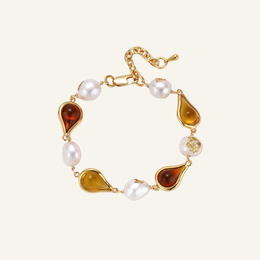 Elegant bracelet with alternating baroque pearls and amber teardrop gemstones set in 18k gold-plated copper on cream background.