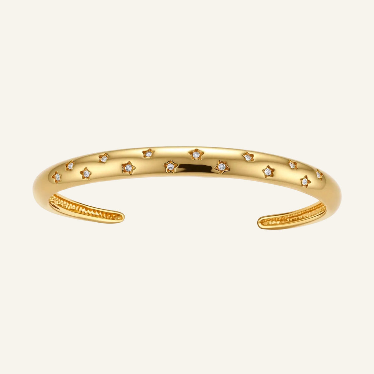 Polished 18K gold plated cuff bracelet with cubic zirconia set in star motifs on a cream background.