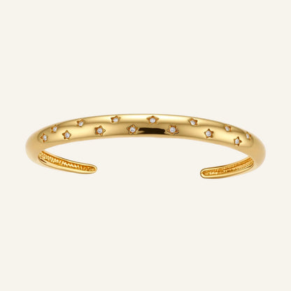 Polished 18K gold plated cuff bracelet with cubic zirconia set in star motifs on a cream background.
