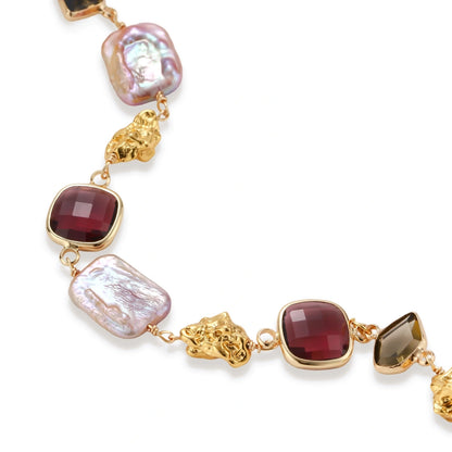 18k gold-plated copper bracelet with burgundy stones, smoky quartz, baroque pearls and ornate golden charms on white background.