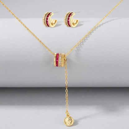 Three-piece jewelry set featuring 14K gold plated pieces with deep red cubic zirconia stones and clear crystals on cream background.