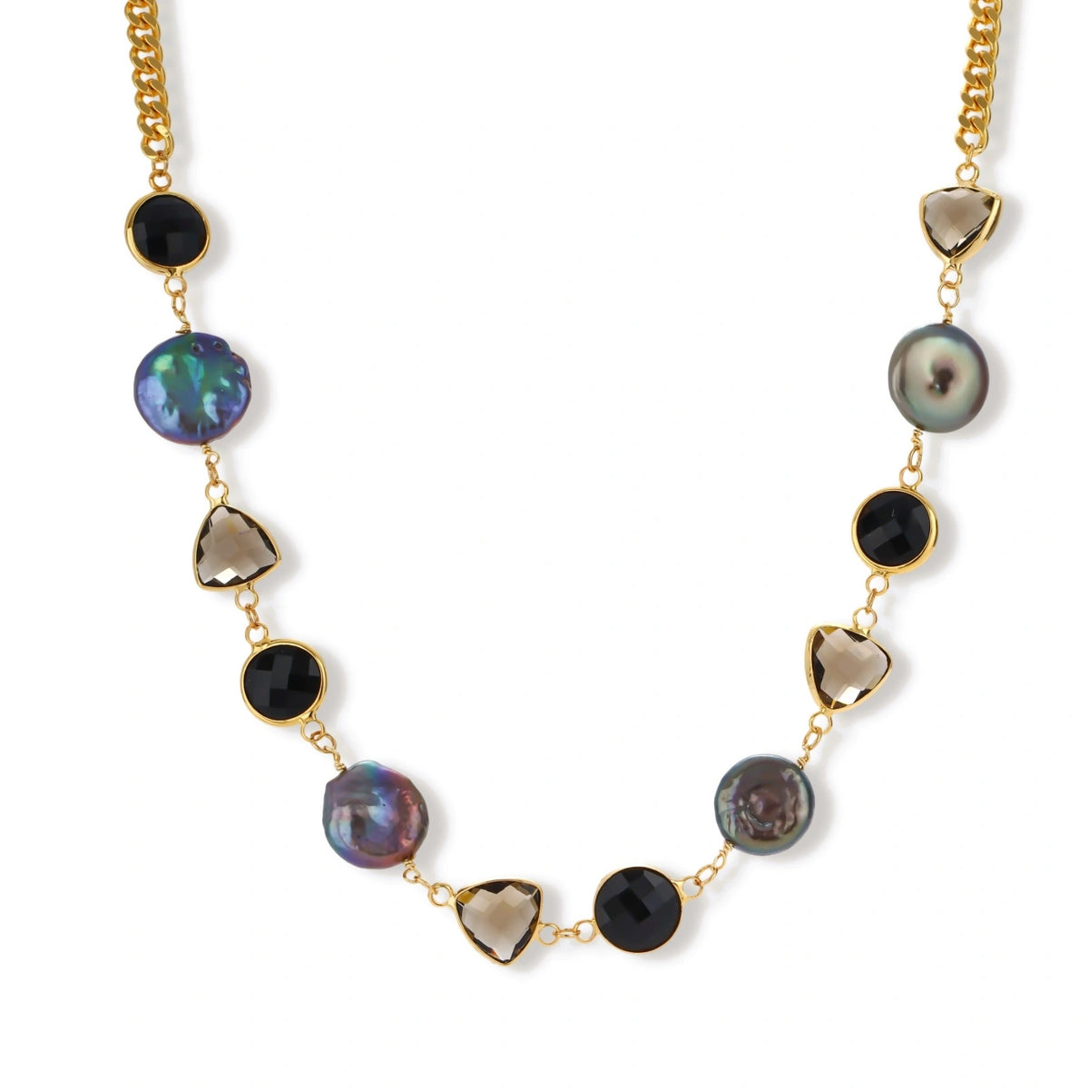 Gold plated curb chain necklace with iridescent baroque pearls, black round stones and smoky triangular stones on a cream background.