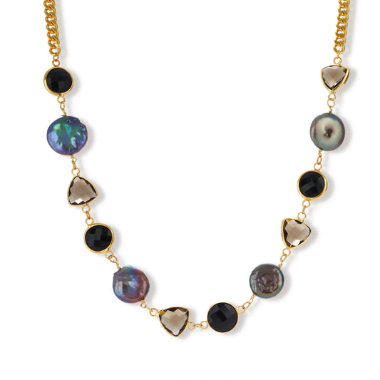 Gold plated curb chain necklace with iridescent baroque pearls, black round stones and smoky triangular stones on a cream background.